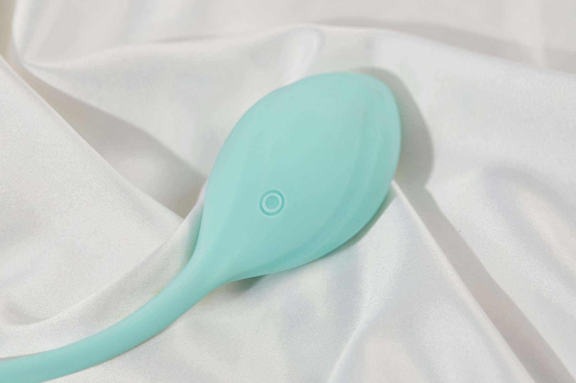 A teal lemon clitoral vibrator on soft white silk fabric