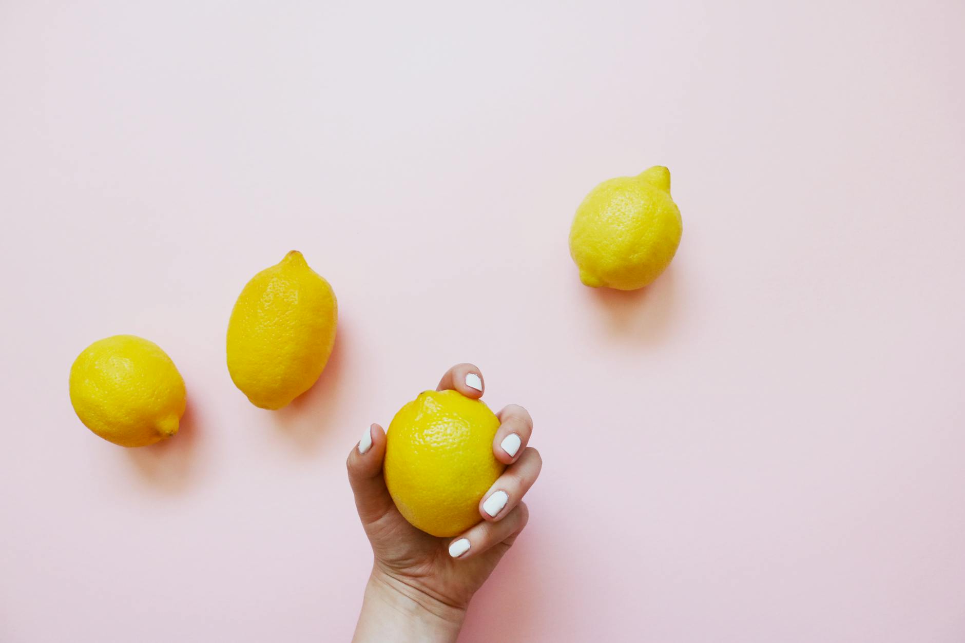 A hand holding a yellow lemon on a soft pink background, symbolizing the variability of perimenopause pleasure