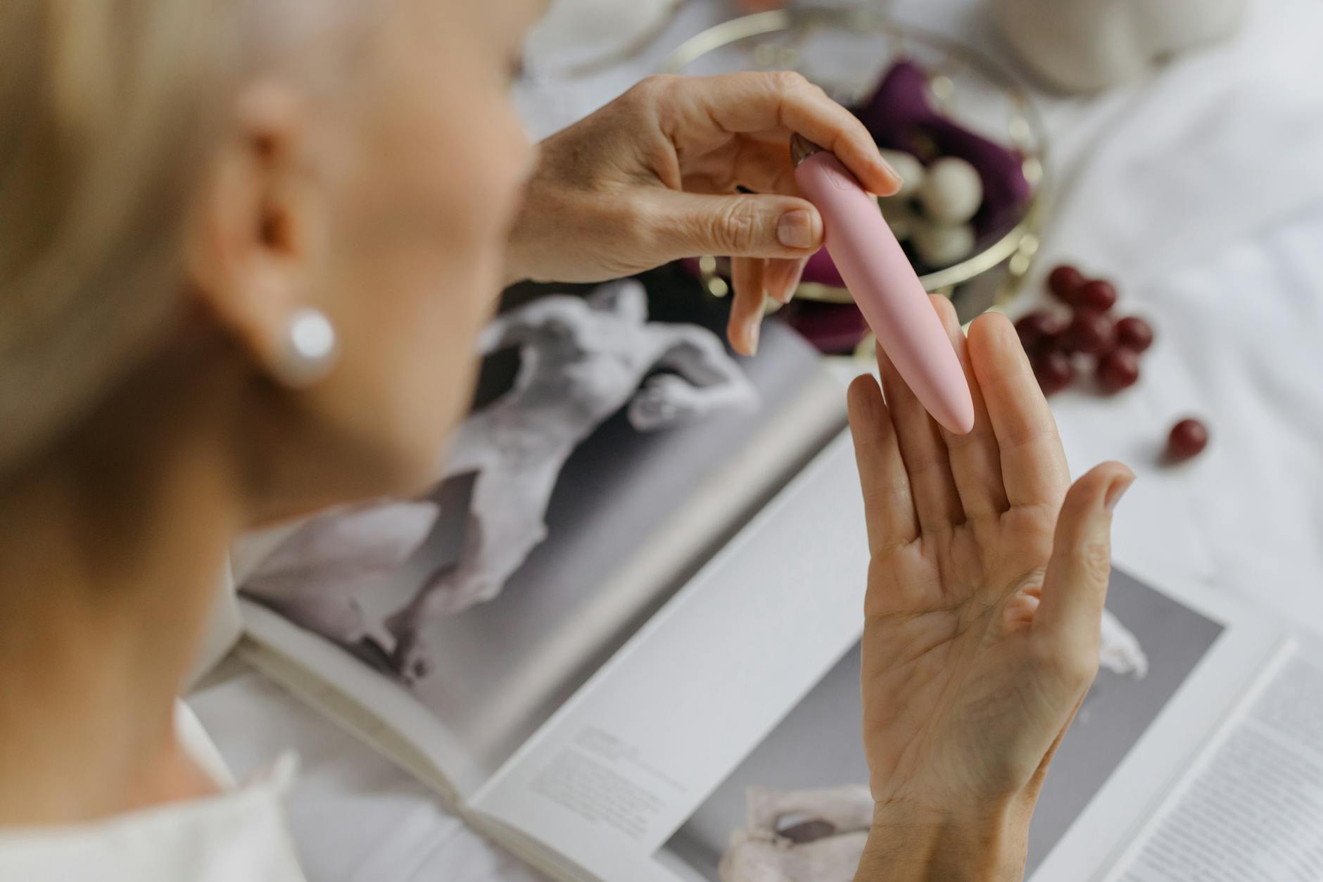 Close-up of a woman holding a pink vibrator, with art books in the background, emphasizing intimate and personal themes