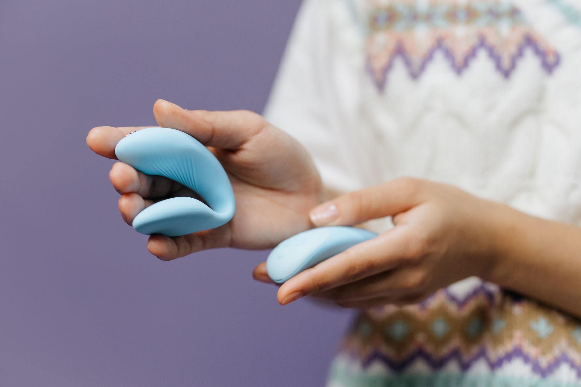 Gros plan d'une personne tenant un vibromasseur bleu et ergonomique contre un fond violet
