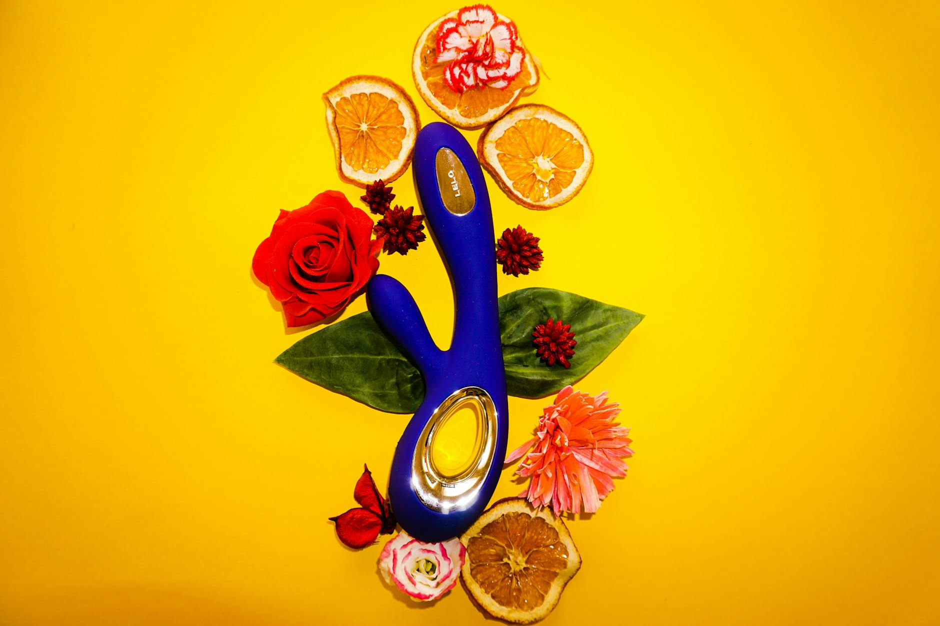 Lemon clitoral vibrator surrounded by fresh citrus and flowers on a bright yellow background